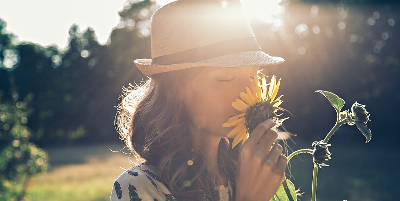 Kvinna står på en äng och doftar på en blomma