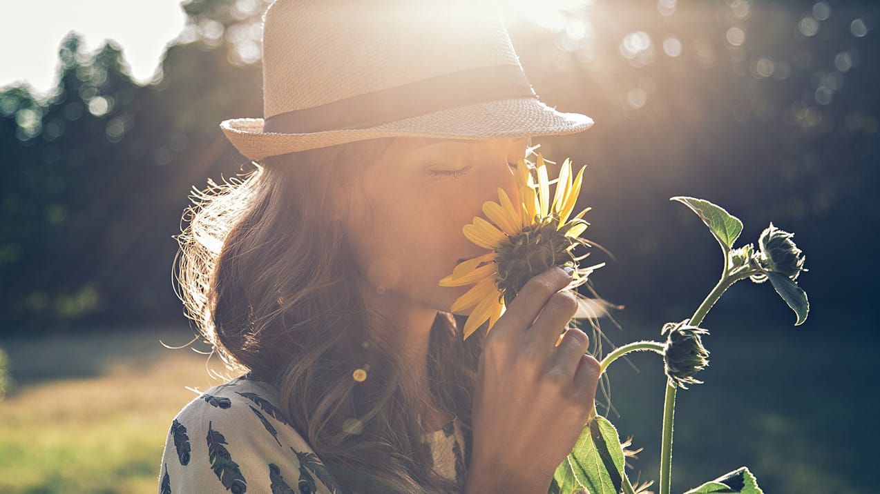 En kvinna står på en äng och doftar på en blomma