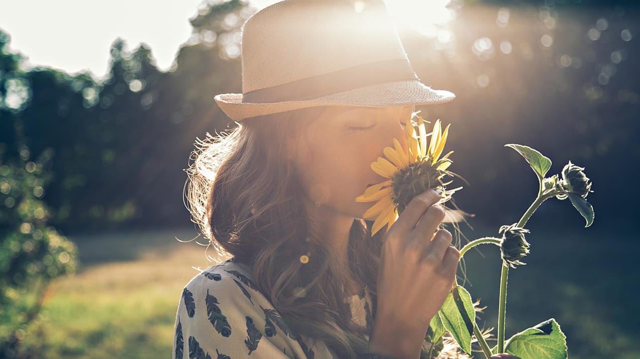 Kvinna står på en äng och doftar på en blomma