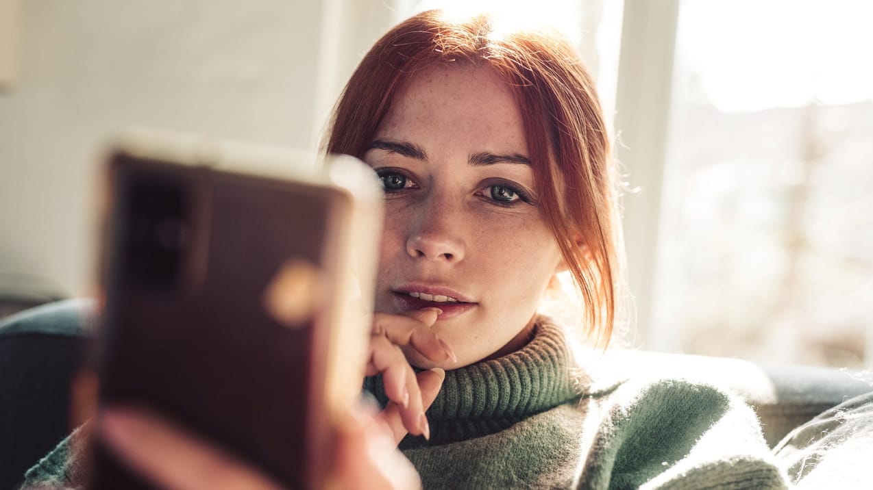 Rödhårig tjej som sitter med sin telefon i handen