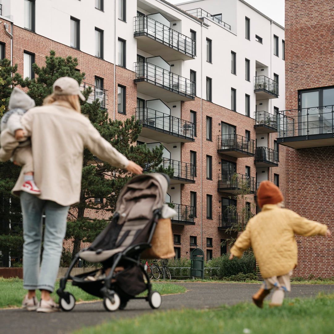 Mamma och barn står i en grönska utanför ett bostadsområde