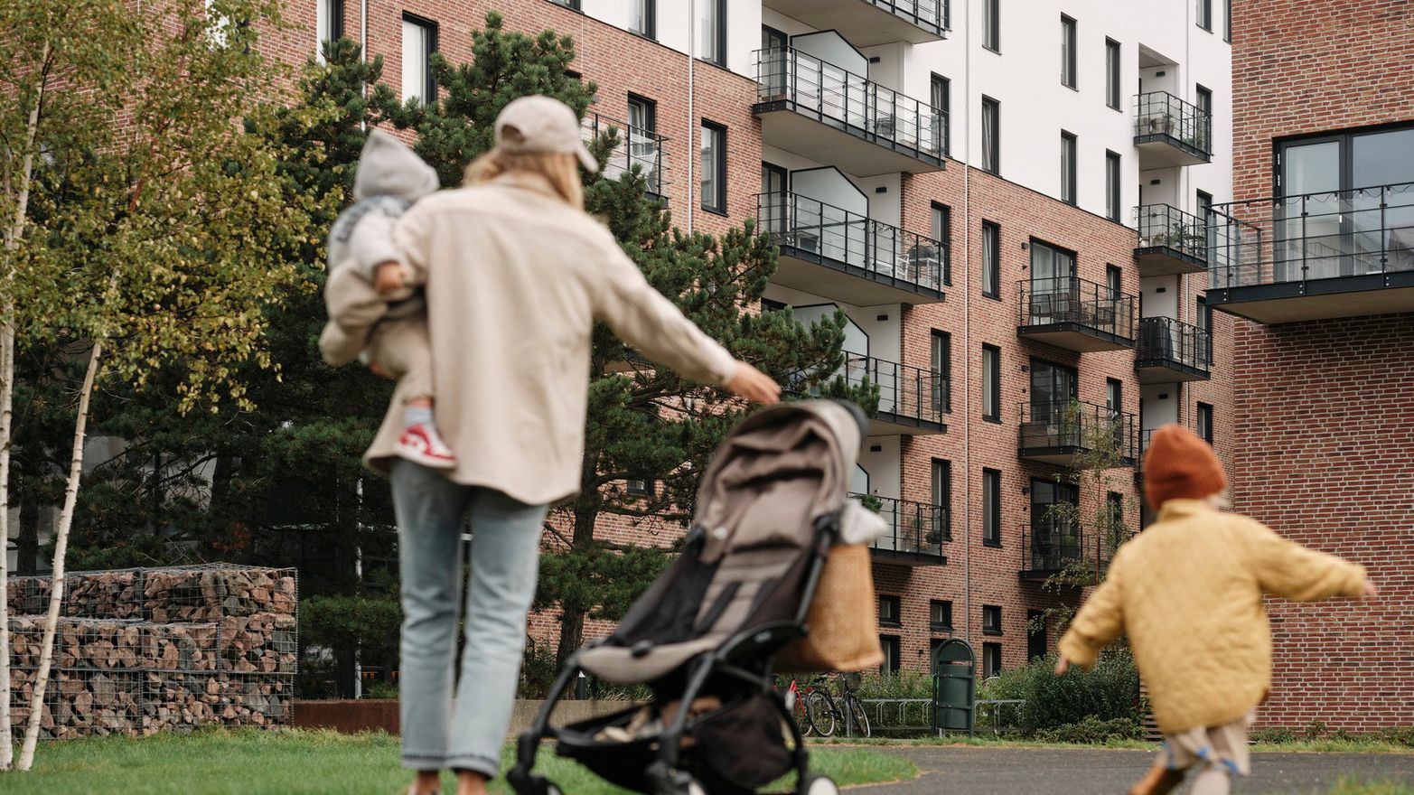 Mamma och barn står i en grönska utanför ett bostadsområde