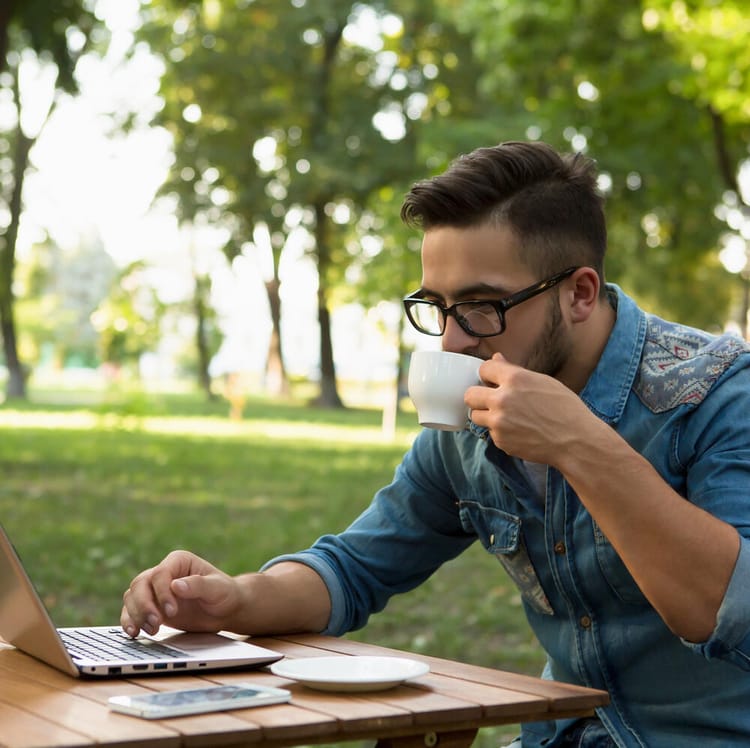 Man sitter i en park med sin laptop och dricker kaffe