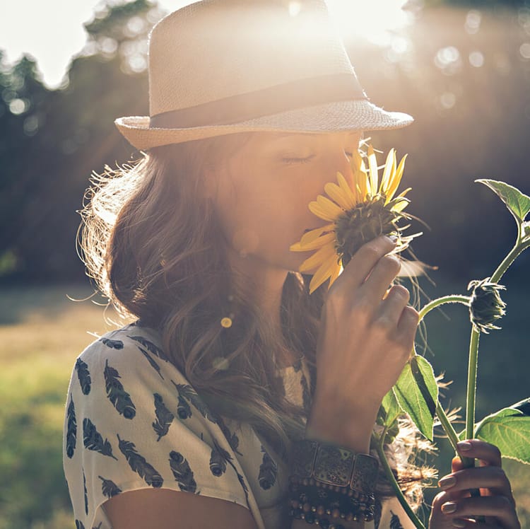 Kvinna står på en äng och doftar på en blomma