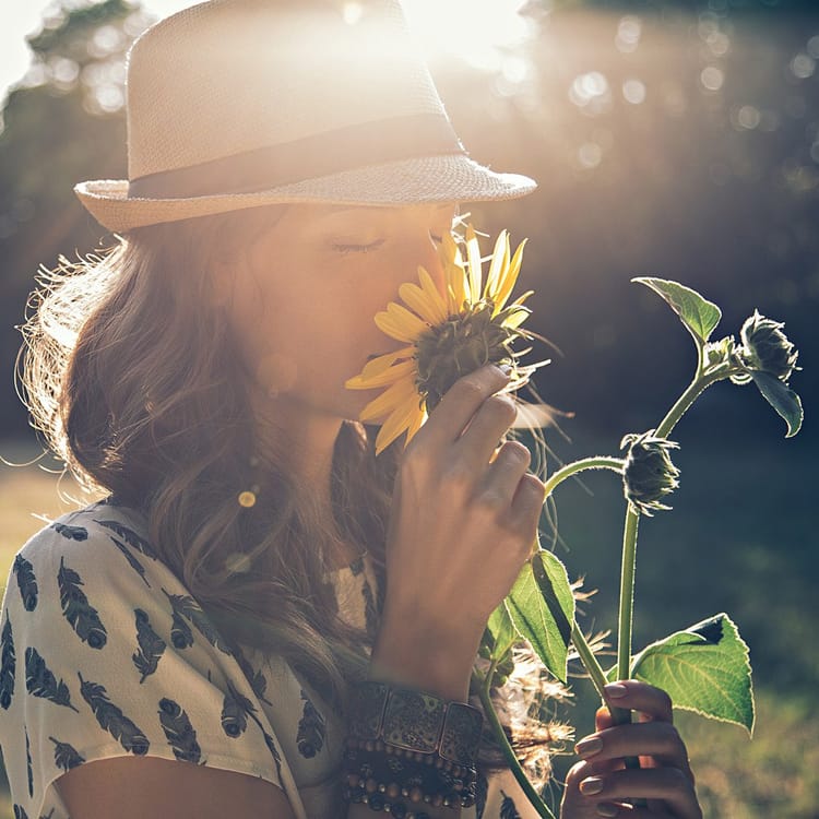 En kvinna står på en äng och doftar på en blomma