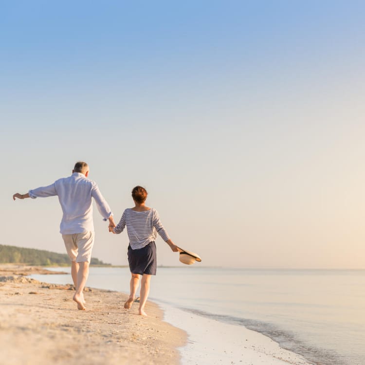 Ett äldre par går hand i hand på stranden