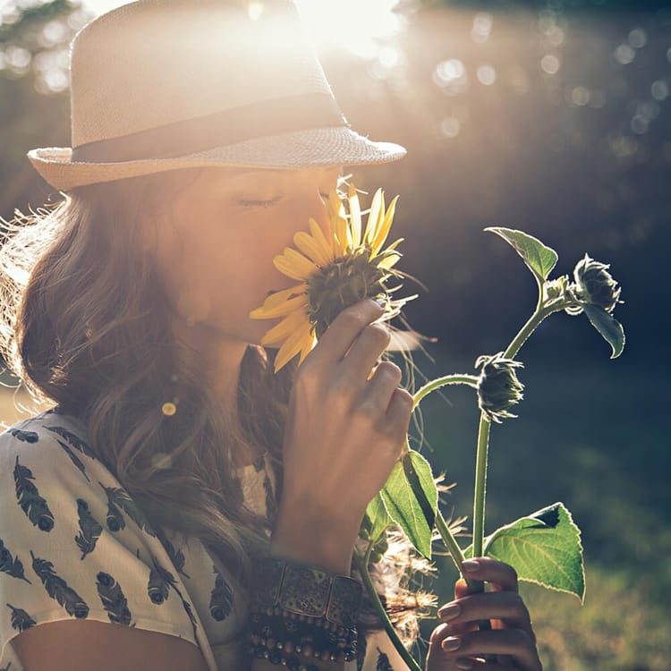 Kvinna står på en äng och doftar på en blomma